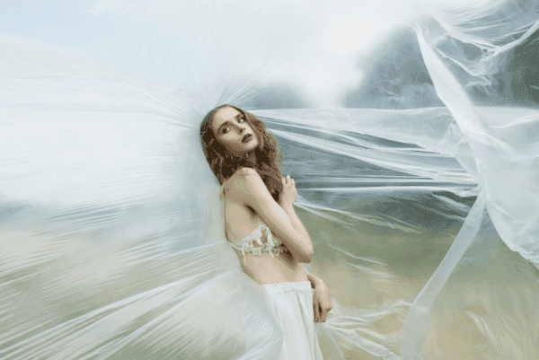 Fashion photographer in a flowing white dress, captured mid-movement against a soft, ethereal backdrop.